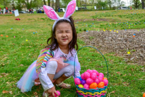 little girl with bunny ear headband and basket full of colored plastic eggs.