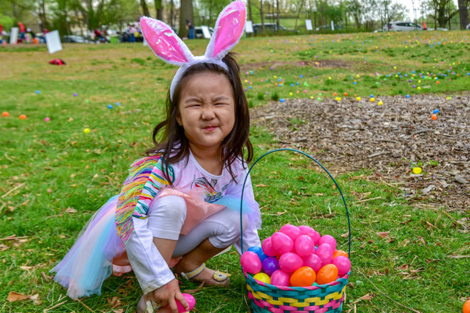 little girl with bunny ear headband and basket full of colored plastic eggs.