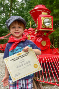 child smiling in front of train holding certificate