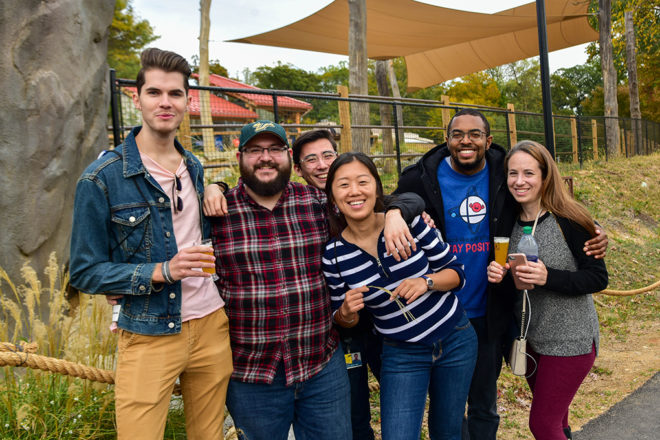 group of people with beer mugs in front of giraffe habitat