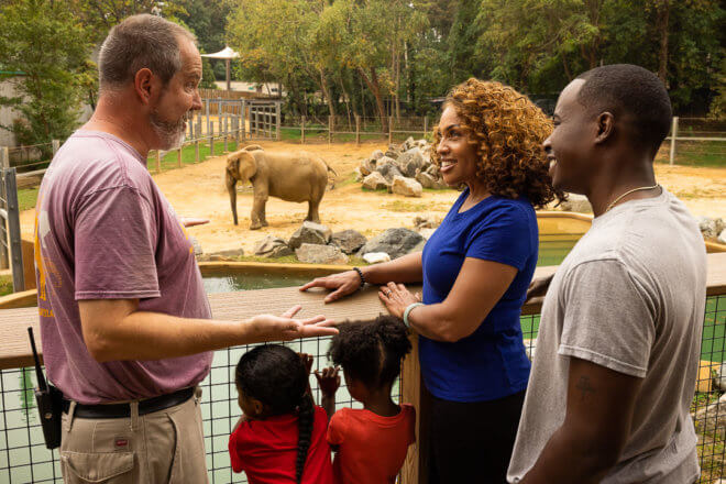 keeper speaking to a family with an elephant behind