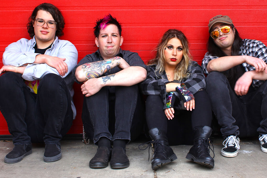 guyliner band members sitting against red wall